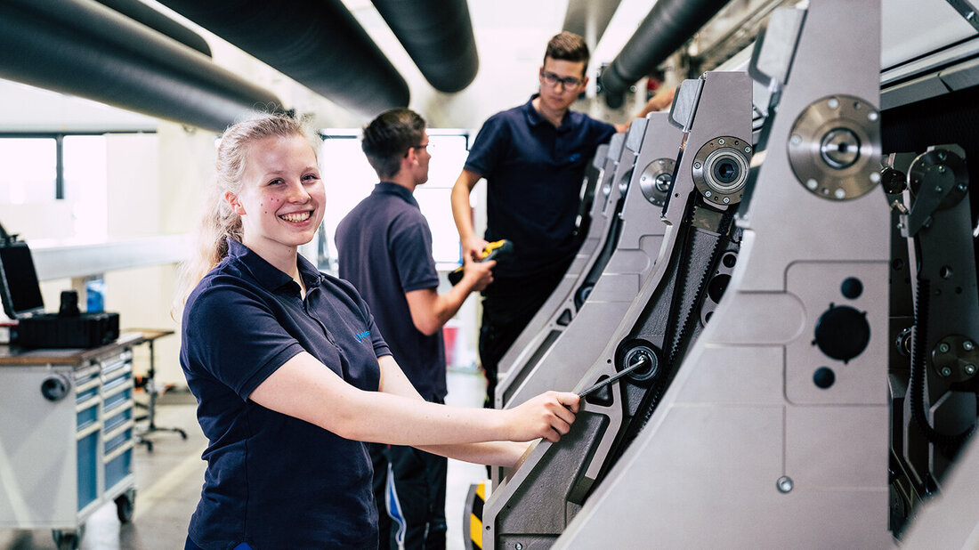 young female trainee stands smiling in front of a machine